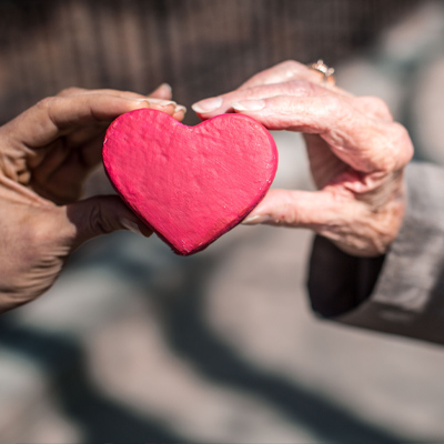 Elderly and younger woman's hands holding red heart