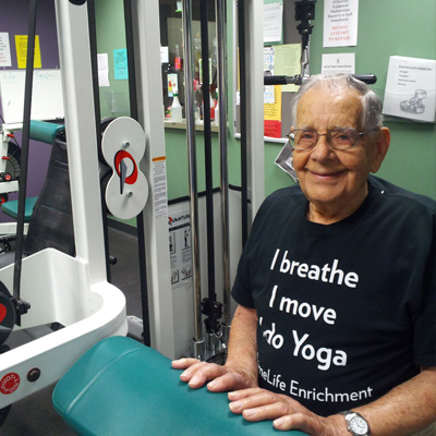 Elderly man smiling while sitting at weight machine in gym