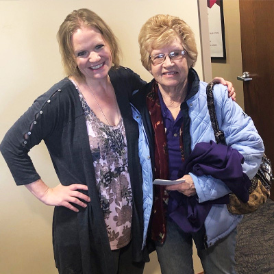 Elderly woman and younger woman stand smiling together in office