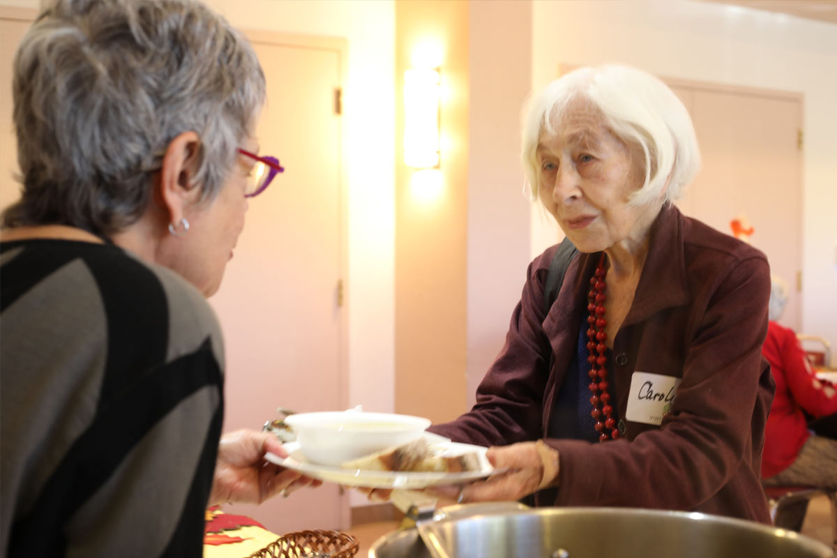 Woman hands a senior woman a warm meal