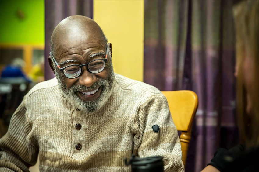 Elderly man smiling while sitting and talking with others