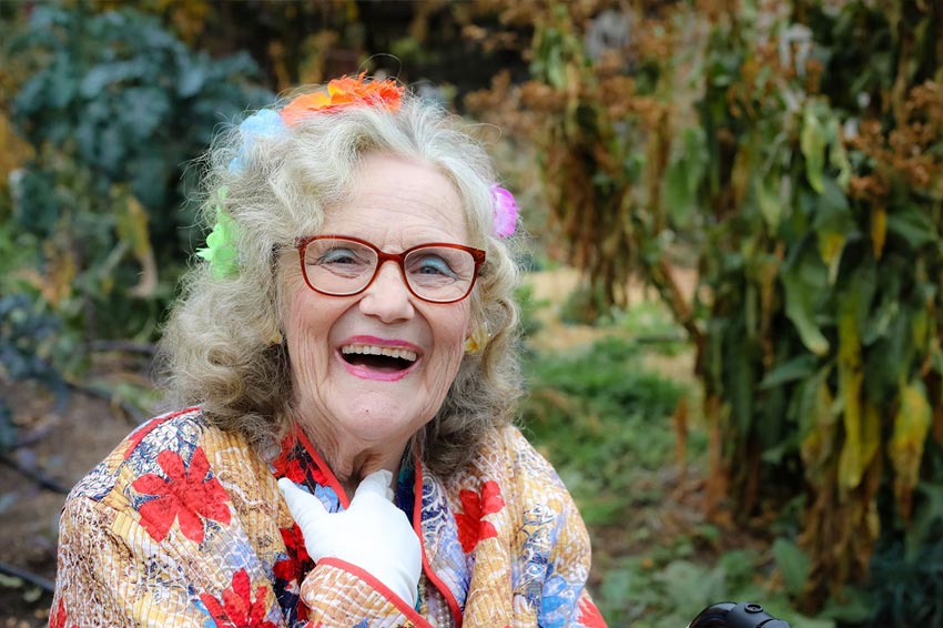 Lavishly dressed senior woman smiles while sitting in outside garden