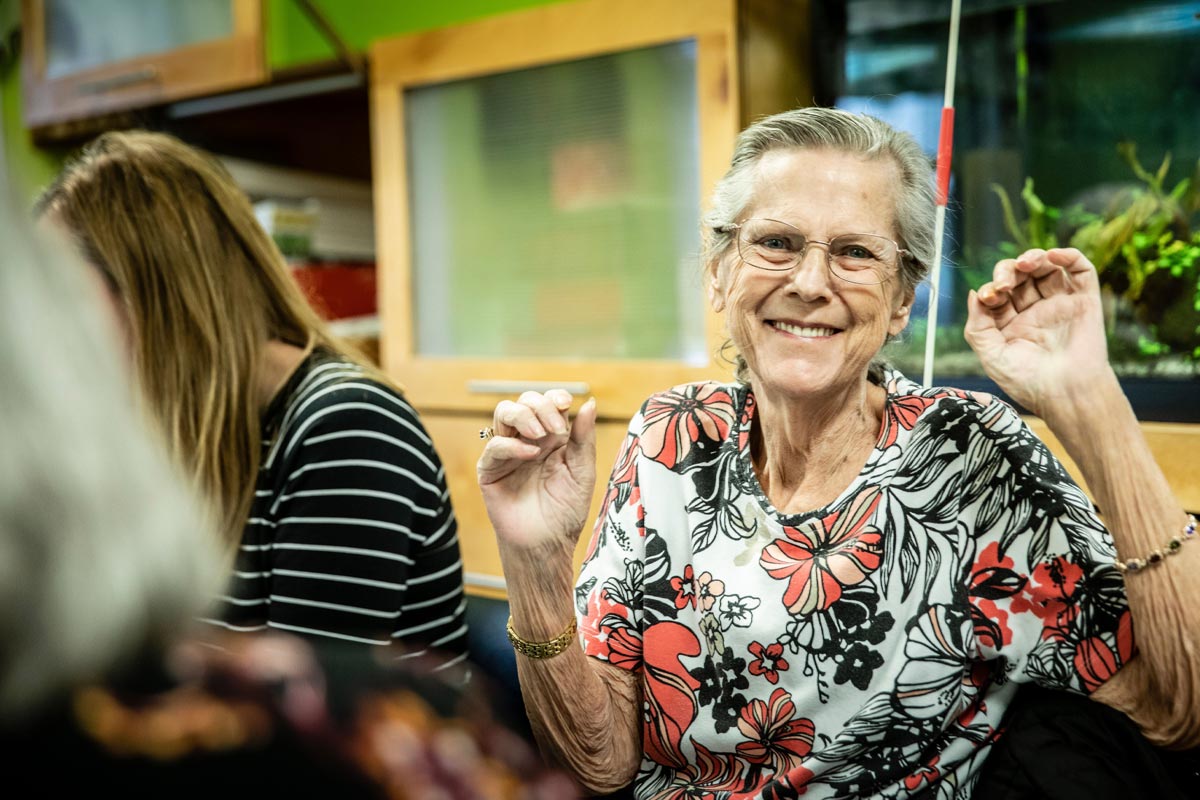 Senior woman smiles while sitting and talking at a table with others